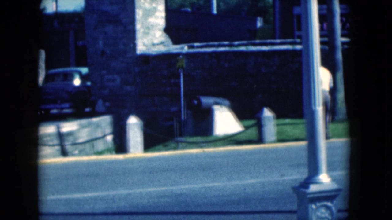 Stone building across a road with parked vintage cars and a lamppost in front.