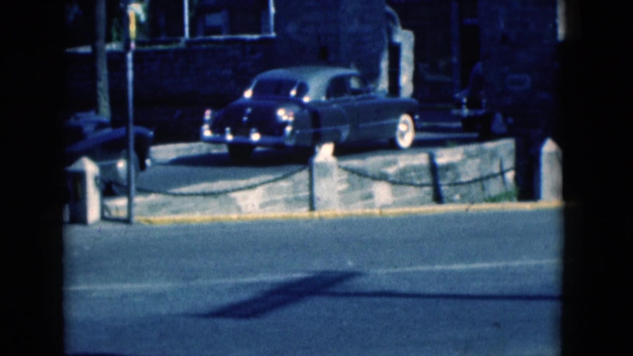 1975 Florida 8mm frame showing a mid-century car by a curb near a building, with street pavement in the foreground.