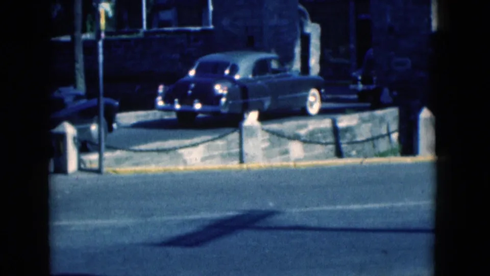 1975 Florida 8mm frame showing a mid-century car by a curb near a building, with street pavement in the foreground.