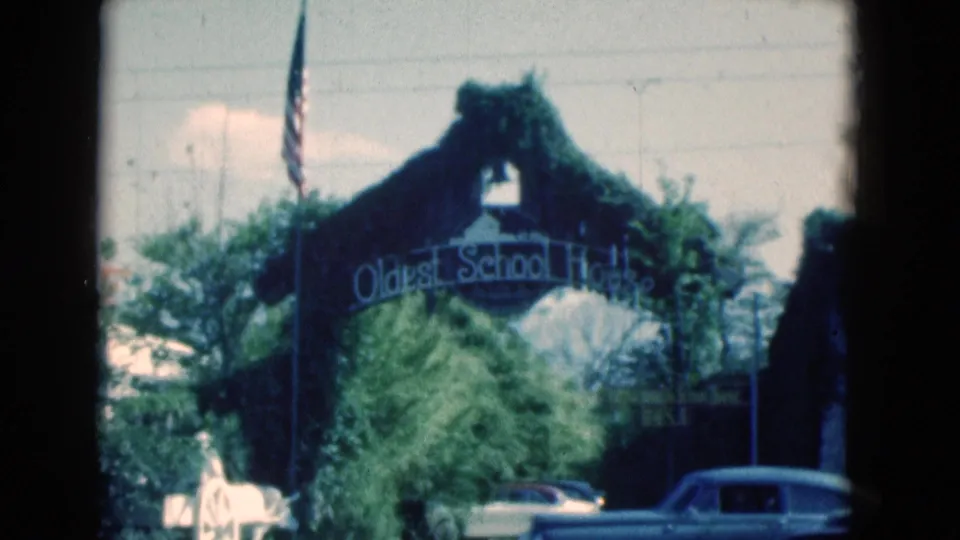 1975 Florida 8mm view of the Oldest School House arch framed by trees, with an American flag and cars at street level.