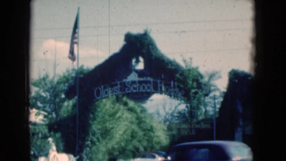 1975 Florida home-movie frame showing the Oldest School House arch as a dark car crosses the foreground.