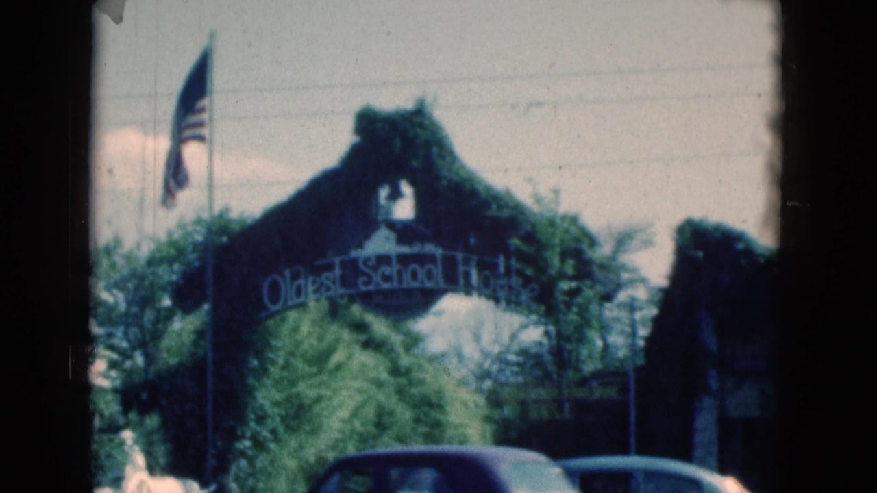 1975 Florida 8mm frame showing the Oldest School House arch, American flag, trees, and a dark car along the street.