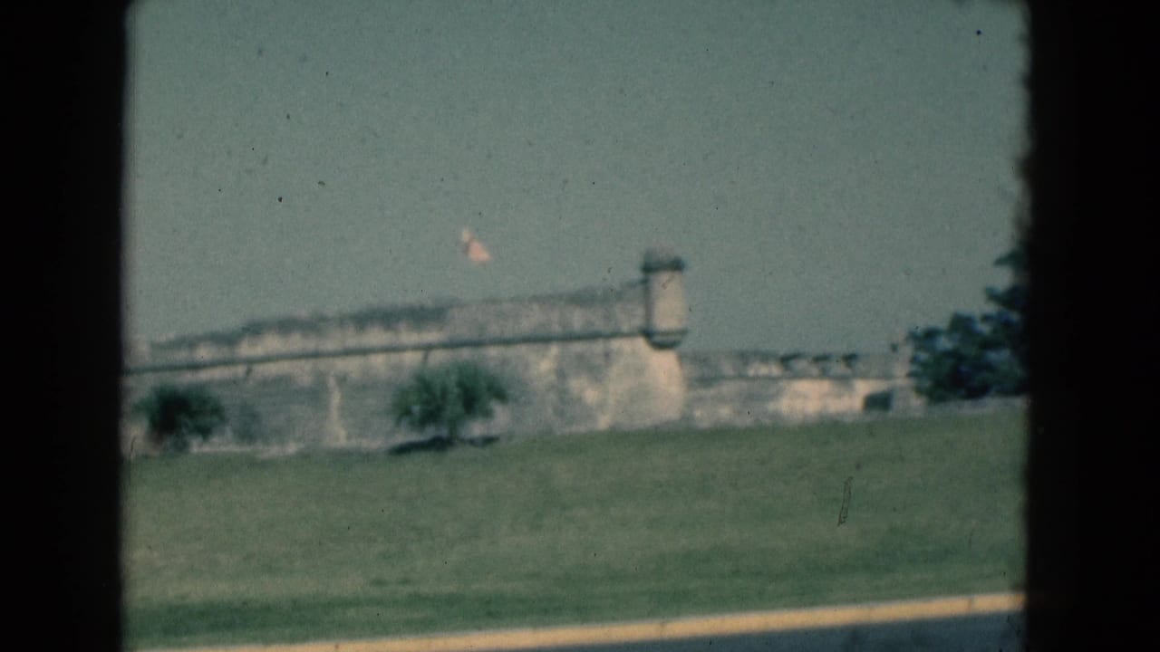 Stone fort and flag beyond a grassy lawn, framed by dark film borders.