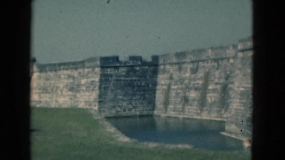 Soft 8mm frame of the Florida stone fortification with a dark wall recess, moat water, grass, and bright sky.