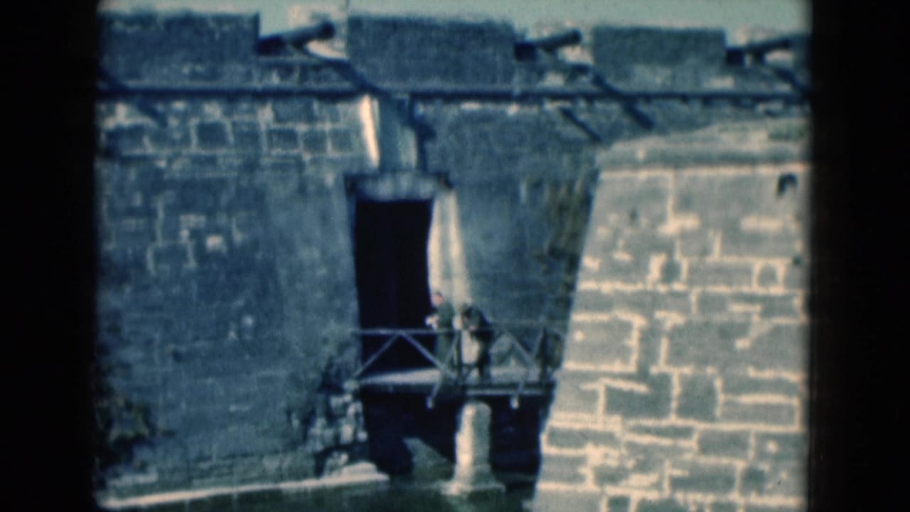 1975 Florida home-movie view of visitors near a small bridge beside a stone fort wall and moat.