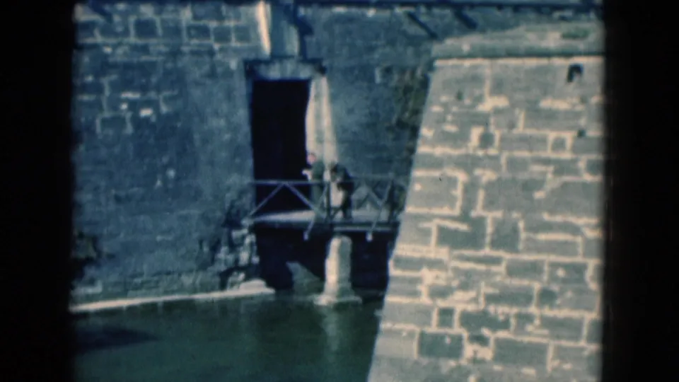 1975 Florida 8mm frame showing a weathered stone fort wall, dark doorway, bridge railing, and moat water.