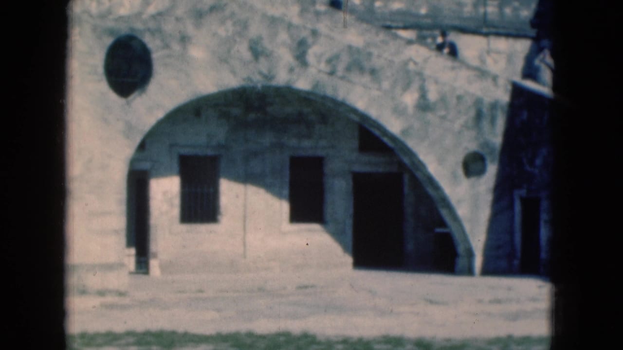 1975 Florida 8mm view of an old weathered facade with a large arch, round wall openings, barred window, and dark doorways.