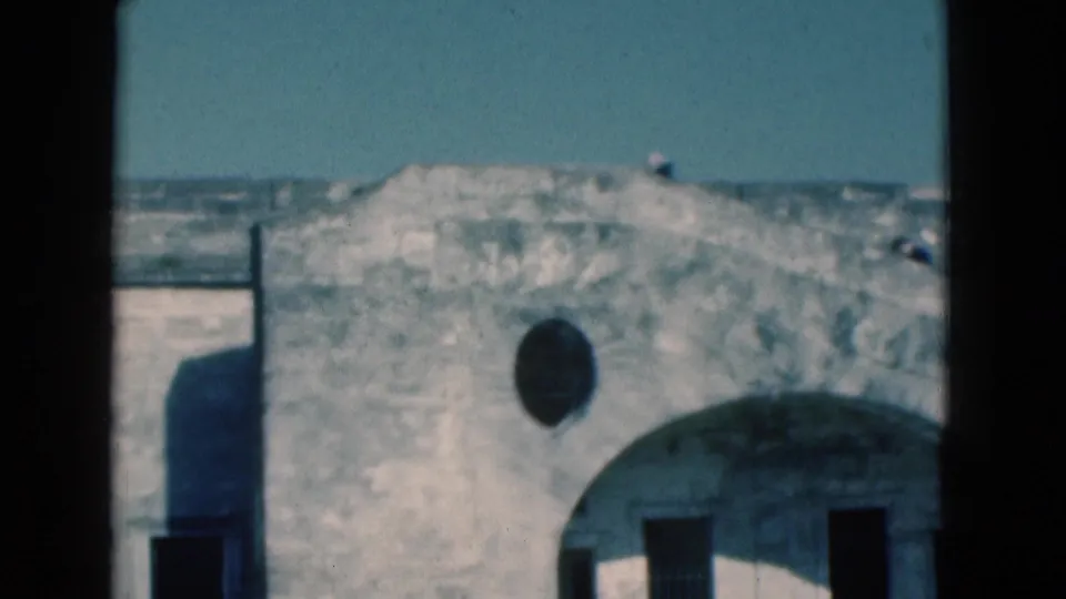 1975 Florida 8mm frame showing a weathered building top, a large arch, a round wall opening, and tiny distant figures on the roofline.