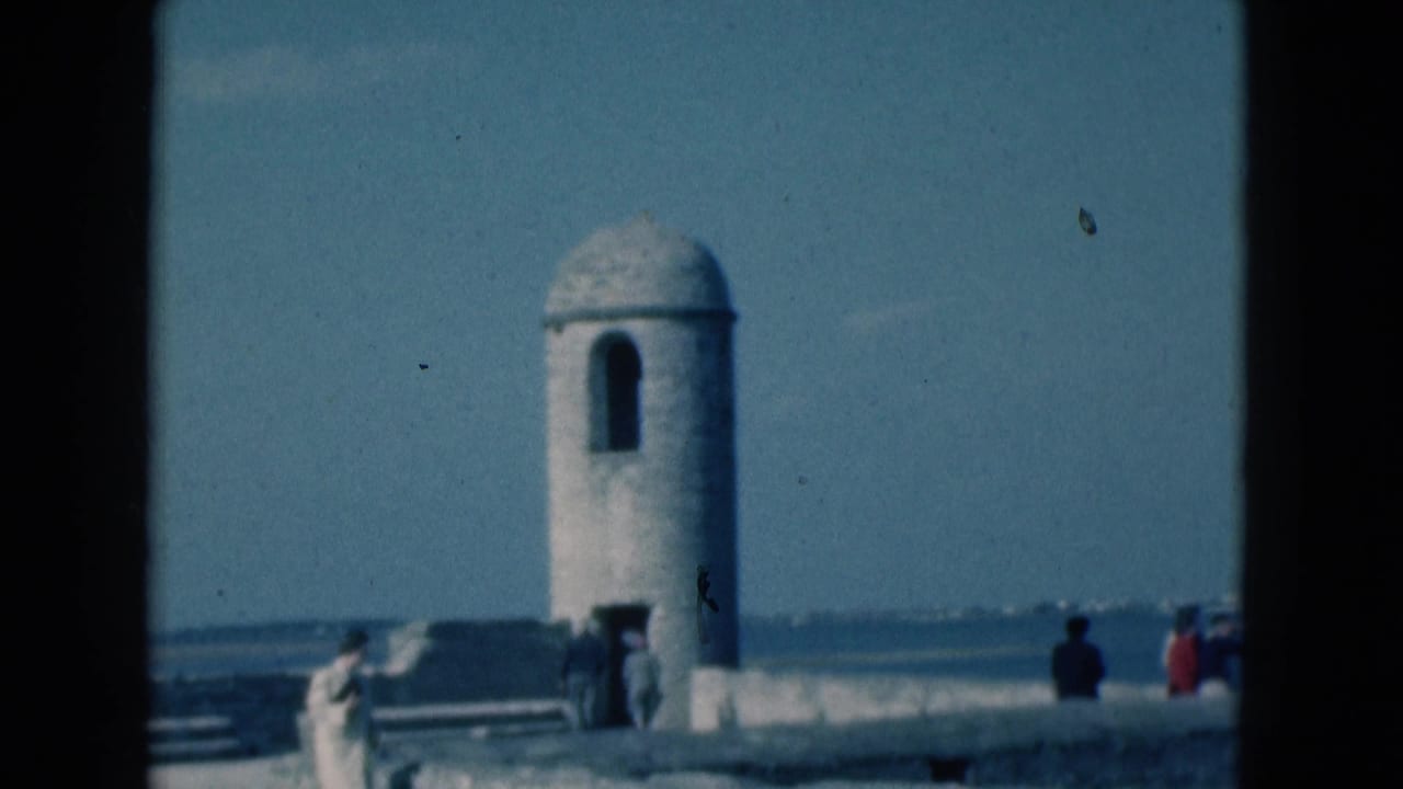 White domed sentry tower beside a stone wall with visitors and ocean in the background.