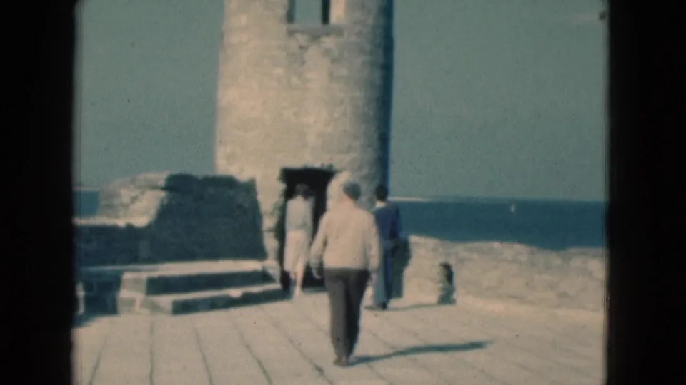 1975 Florida vacationers walk across a paved area toward the arched doorway of old stone fort ruins.