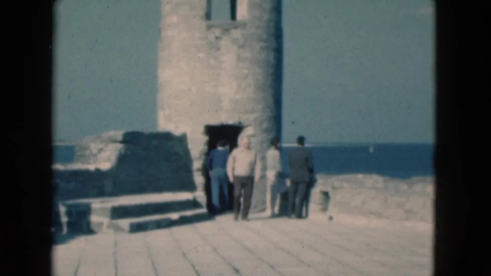 1975 Florida 8mm frame showing tourists repositioning near a coastal ruin tower entrance above the sea.