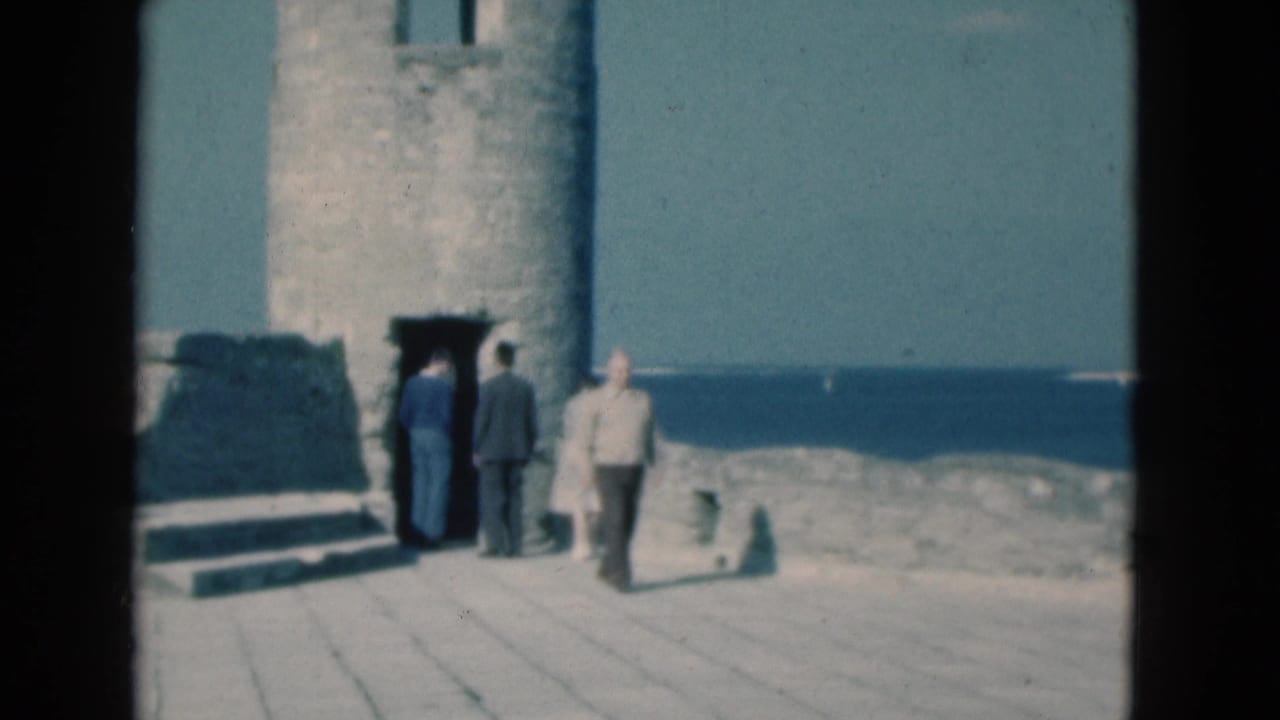 Adults stand and walk beside a lighthouse doorway overlooking the ocean.
