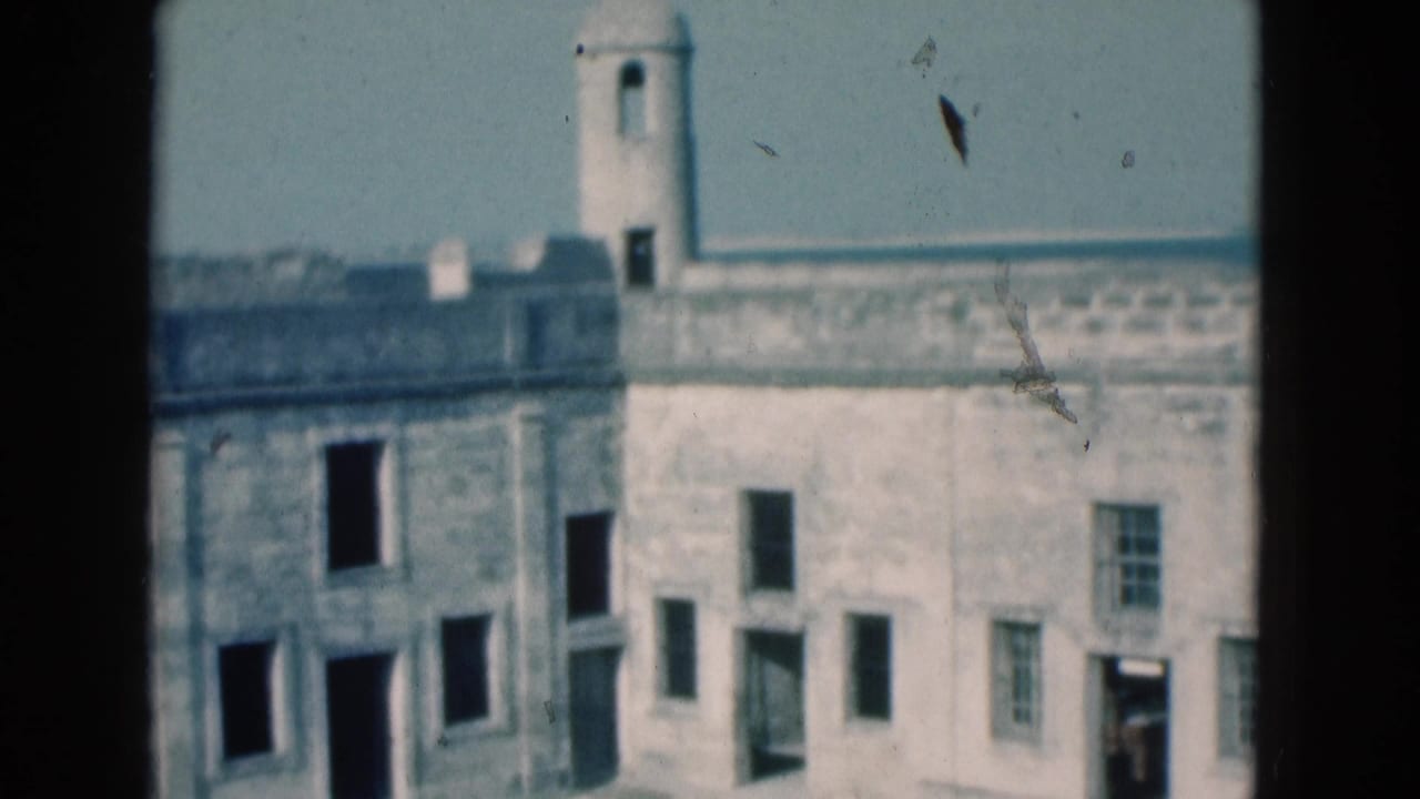 1975 Florida home-movie frame showing a stone fort facade, tower, empty window openings, and sunlit courtyard.