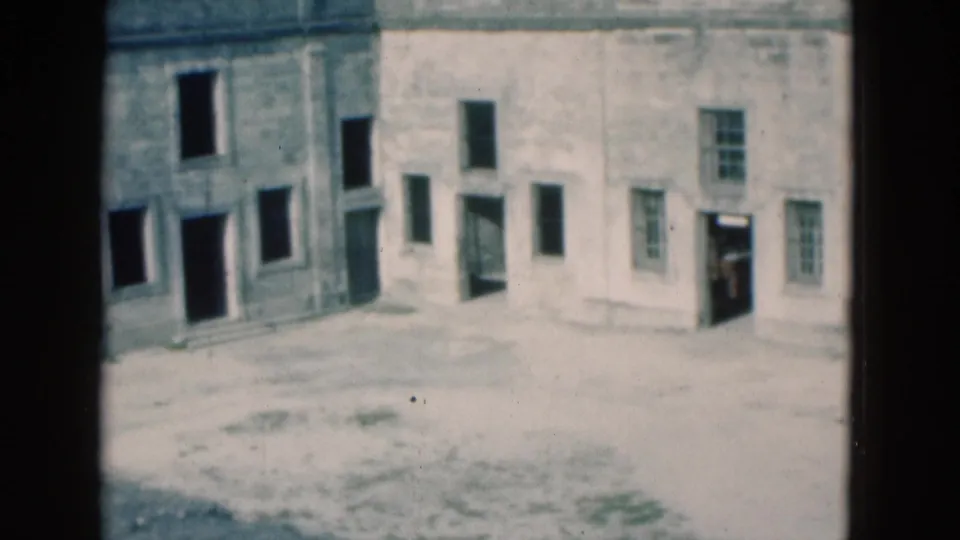 1975 Florida 8mm frame of a fortress courtyard, showing pale masonry, a small tower, open window bays, and a dark doorway.