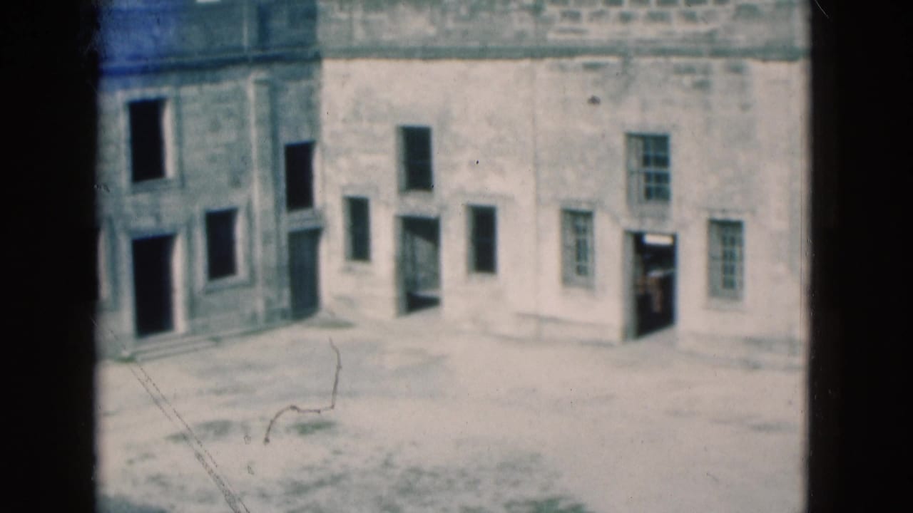 Weathered stone courtyard seen through dark film framing, with small windows and doorways.