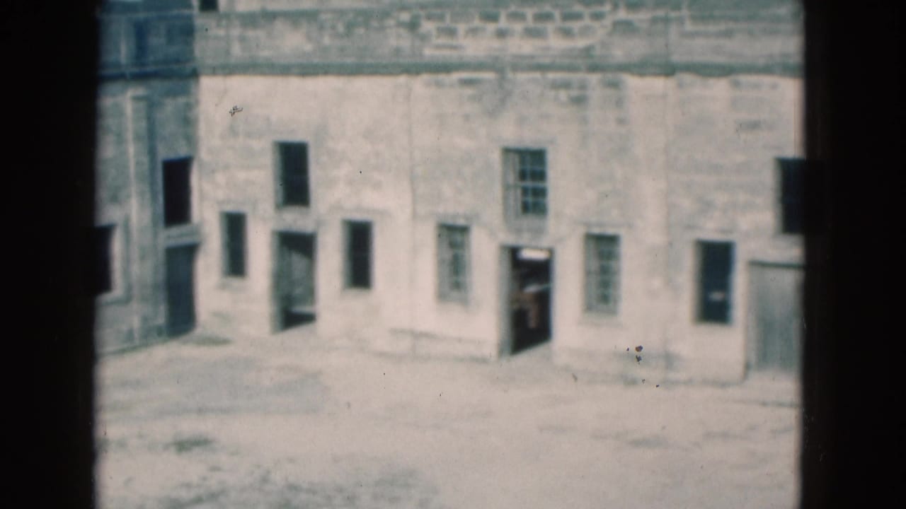 1975 Florida home-movie frame of a historic stone wall with a doorway figure and small windows.