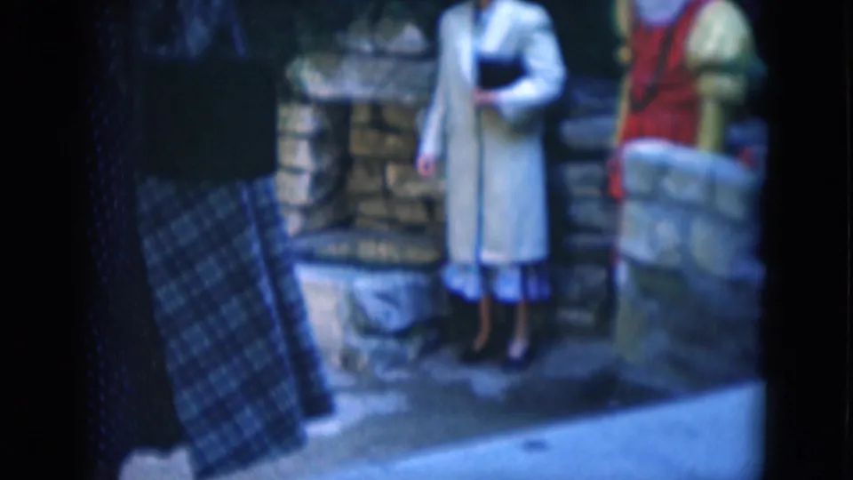 A closer, partly obstructed 8mm frame shows the lower bodies of the costumed figures near stonework, with a dark plaid foreground shape at left.