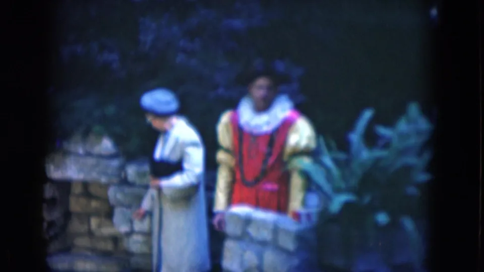 The woman turns or looks downward while the young man in a red and yellow costume stands behind a low stone wall in the Florida 1975 home-movie frame.