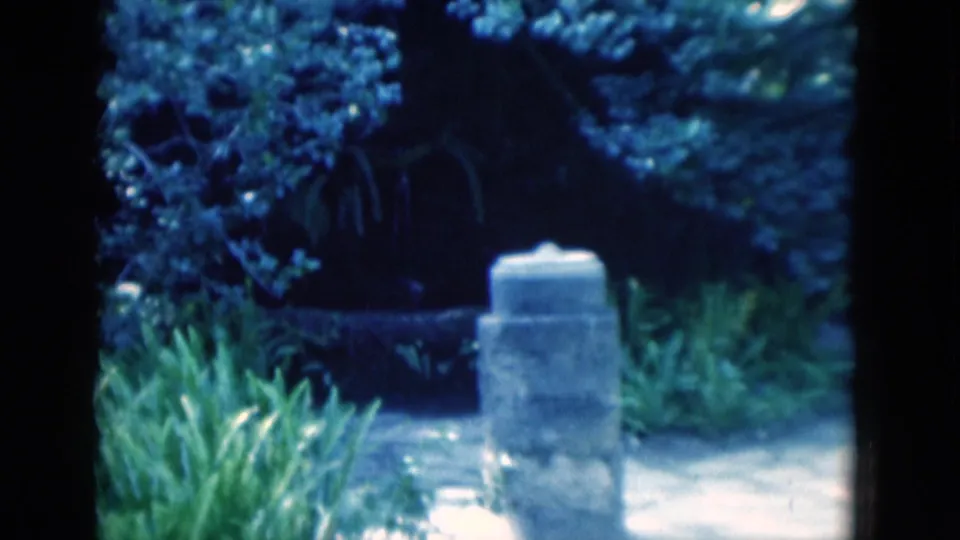 The final frame holds on a stone marker in a lush garden, with shaded plants and path surfaces visible.