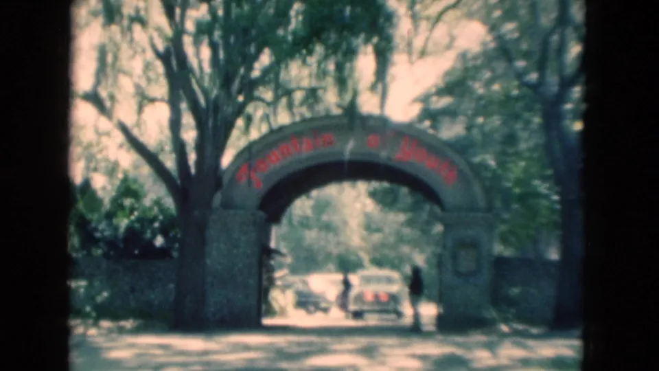 1975 Florida 8mm view of the stone Fountain of Youth arch, with a car near the opening, another vehicle behind it, and a person at right.
