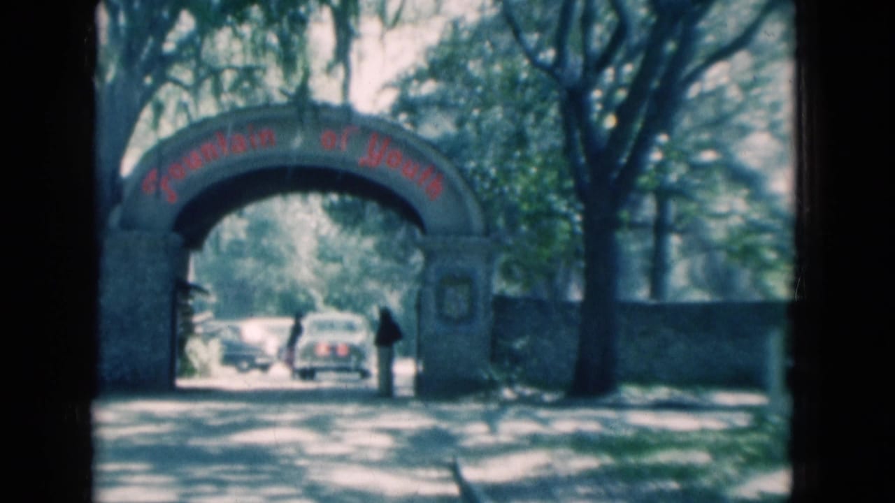 1975 Florida home-movie view of the Fountain of Youth arch, shaded road, cars, and a person standing near the wall.