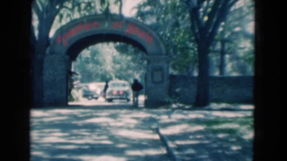 1975 Florida 8mm frame centered on the Fountain of Youth arch, with vintage cars and dappled shade beyond it.