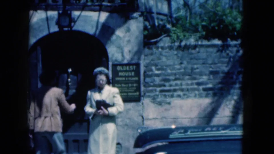 1975 Florida frame showing two women at a doorway near brickwork and a readable Oldest House sign.