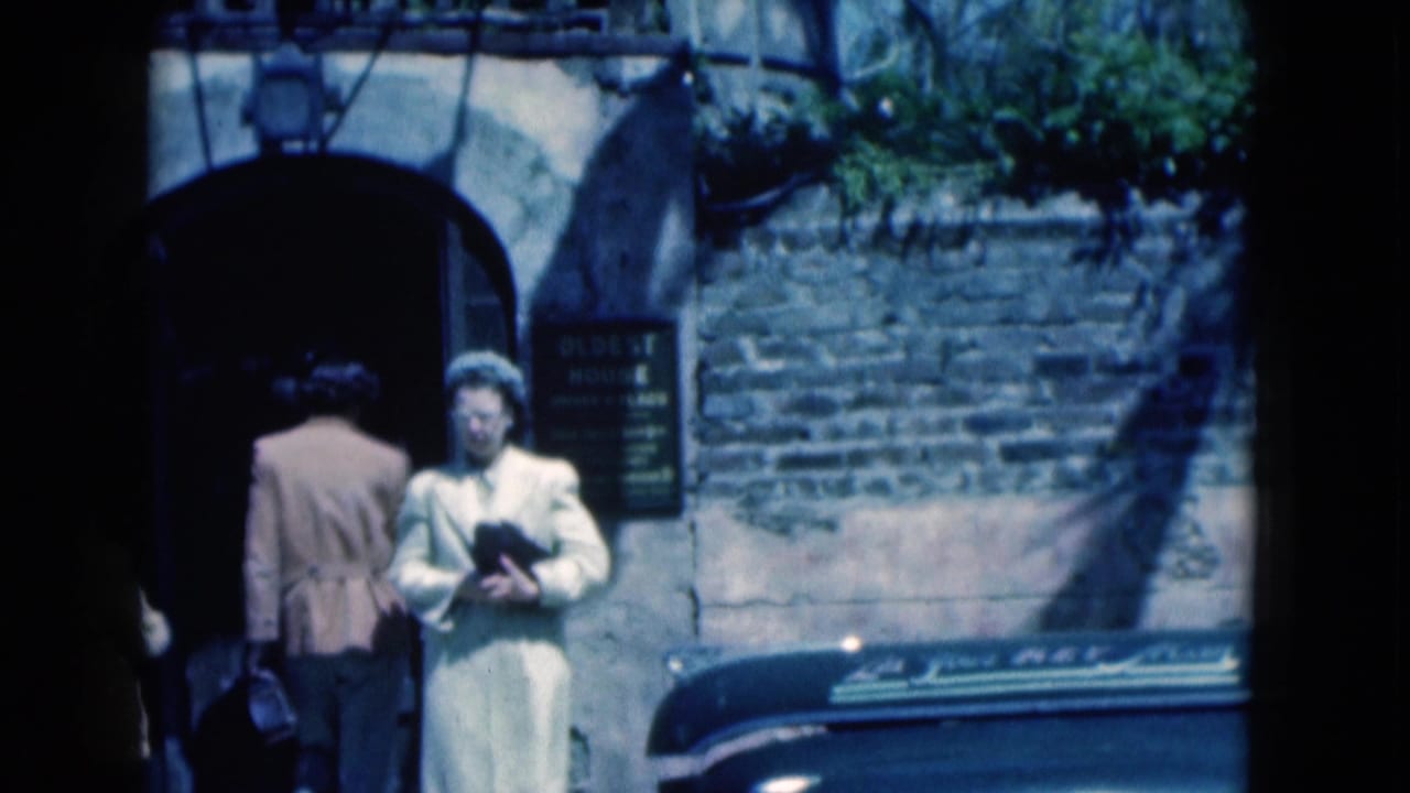 Visitors stand by an arched doorway with an oldest house sign and a car roof in the foreground.