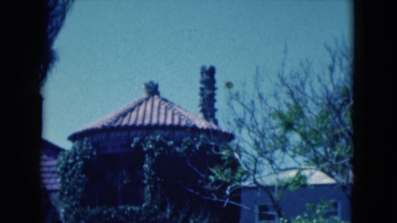 Round ivy-covered building with terracotta roof, chimney stacks, trees, and blue sky.