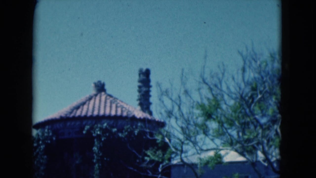 1975 Florida home-movie frame of an ivy-covered round building, chimney stacks, trees, and a pale adjacent structure.