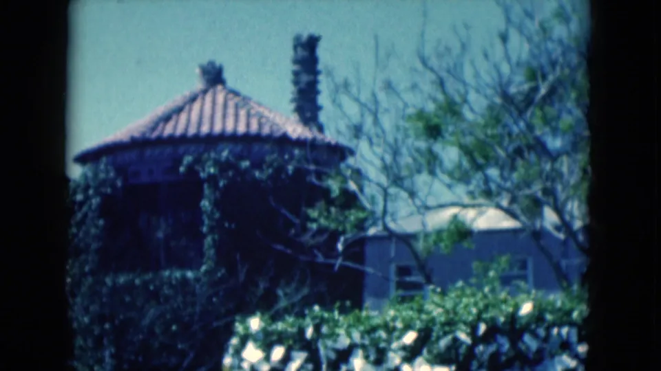 1975 Florida frame showing the ivy-covered round building, terracotta roof, chimney stacks, shrubs, and surrounding trees.