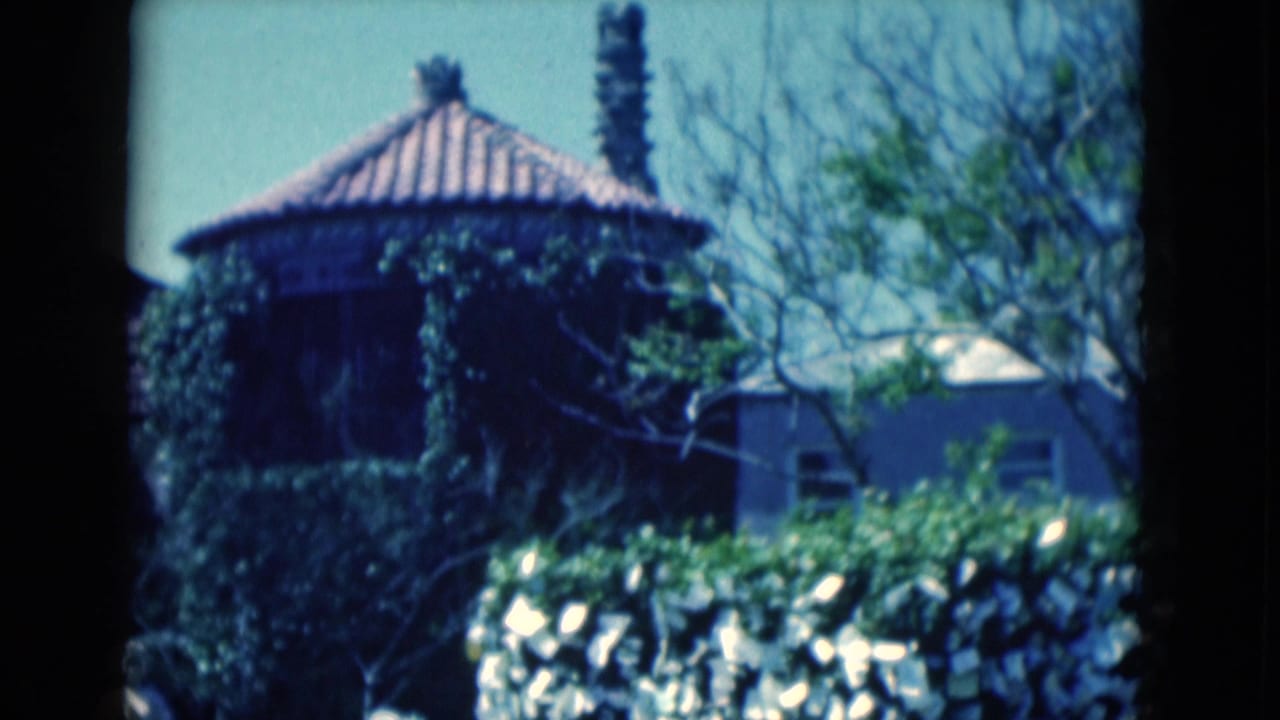 1975 Florida 8mm frame showing an ivy-covered round structure with a tiled roof, trees, and a bright hedge in a landscaped garden.