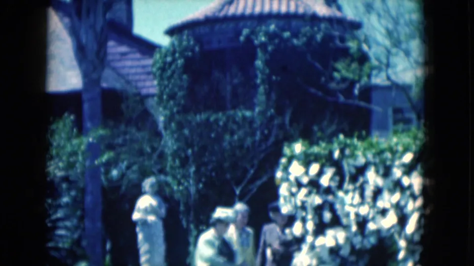 1975 Florida garden view with a white statue on a pedestal, surrounding plants, visitors, and an ivy-covered round building behind it.