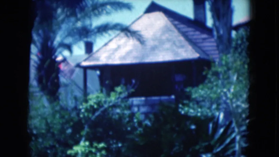 1975 Florida 8mm frame with the residence closer in view, palms and tropical shrubs filling the foreground.