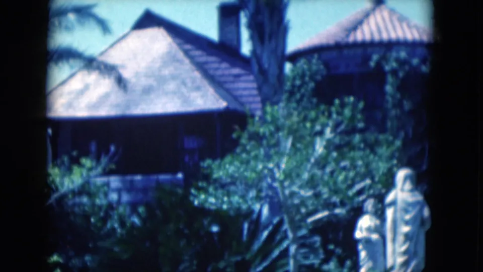 1975 Florida 8mm frame showing a garden pavilion area with dense foliage, a stone wall, and pale statues in the foreground.