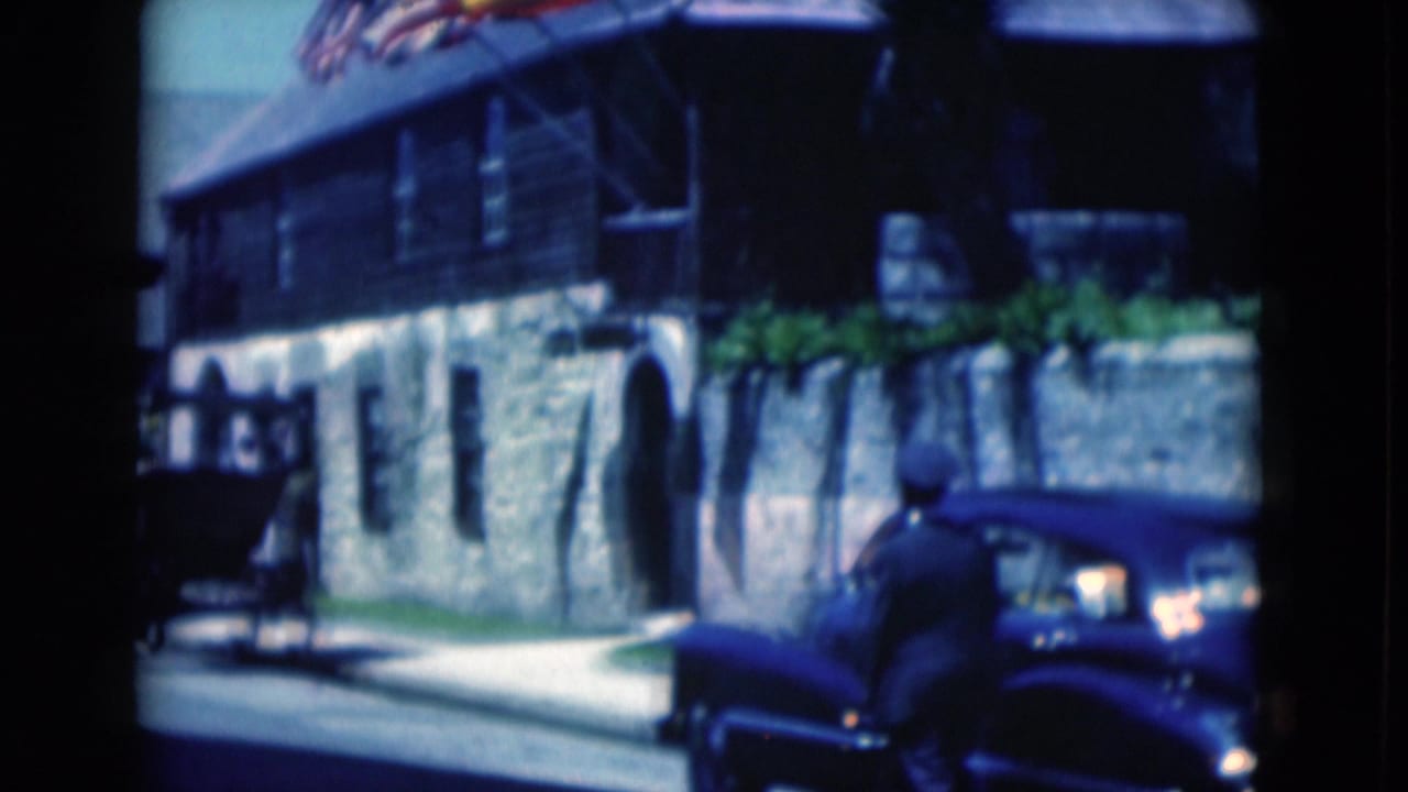 Blue car parked beside a stone building, with a man partly visible near the vehicle.