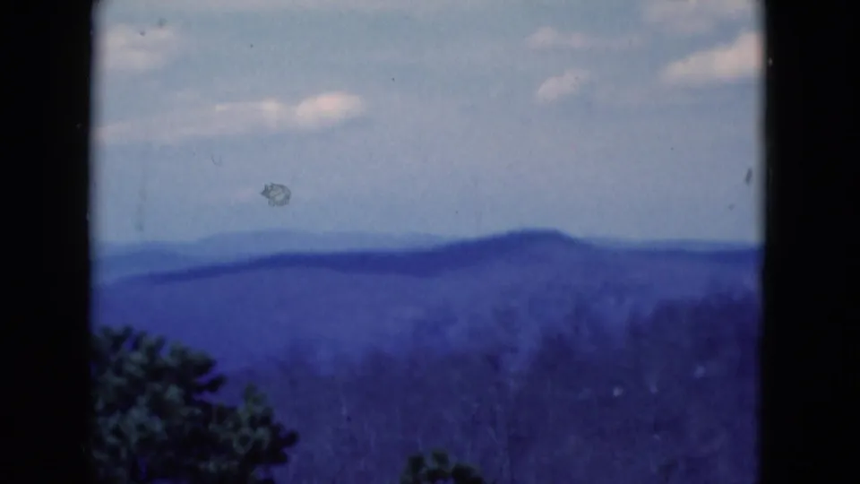 1975 8mm Florida landscape frame with distant blue hills, a pale sky, and dark foreground trees near the lower edge.