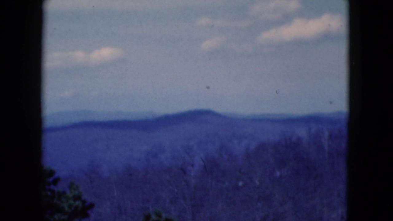 1975 8mm frame of a blue-toned distant hill view under a pale sky, with dark gate edges visible.