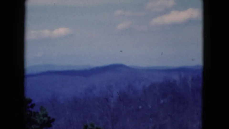 1975 8mm frame of a blue-toned distant hill view under a pale sky, with dark gate edges visible.