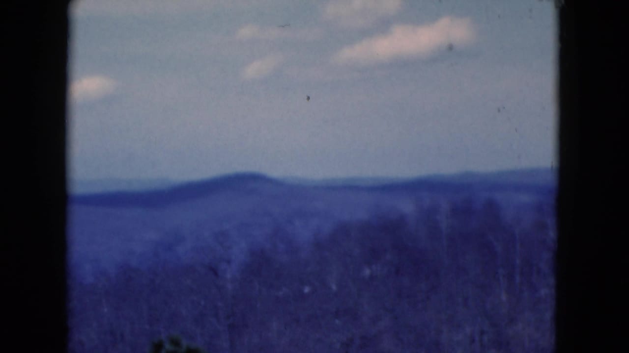 Blue-shifted 8mm view of layered hills and a pale clouded sky, reportedly from Florida in 1975.