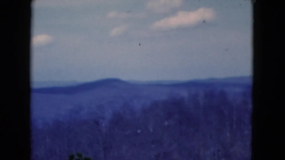 Blue-shifted 8mm view of layered hills and a pale clouded sky, reportedly from Florida in 1975.