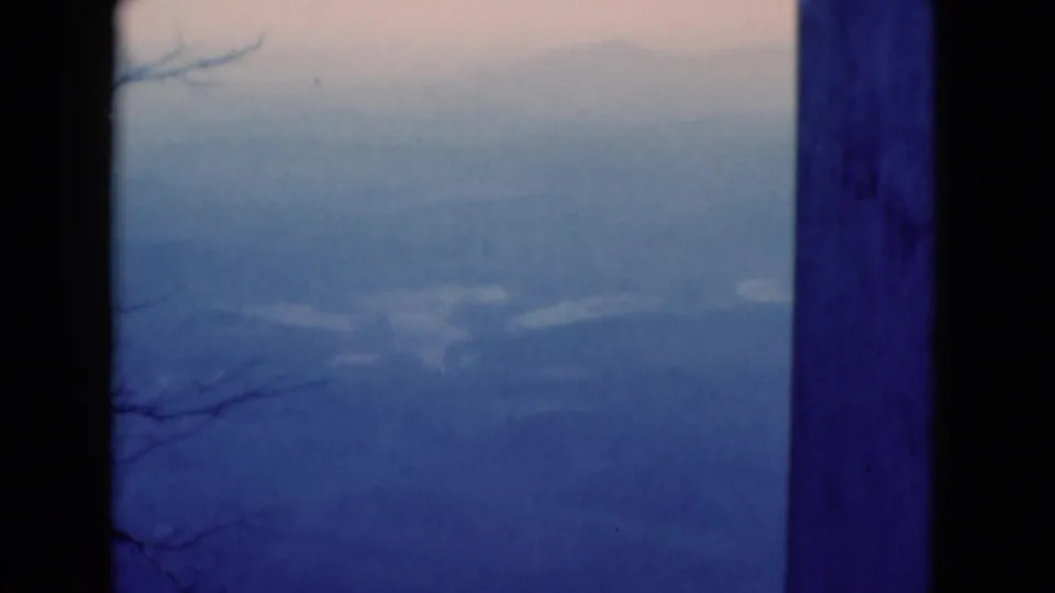 Soft, blue-toned 1975 8mm landscape showing distant hills, bare branches, and a dark vertical post at the side.