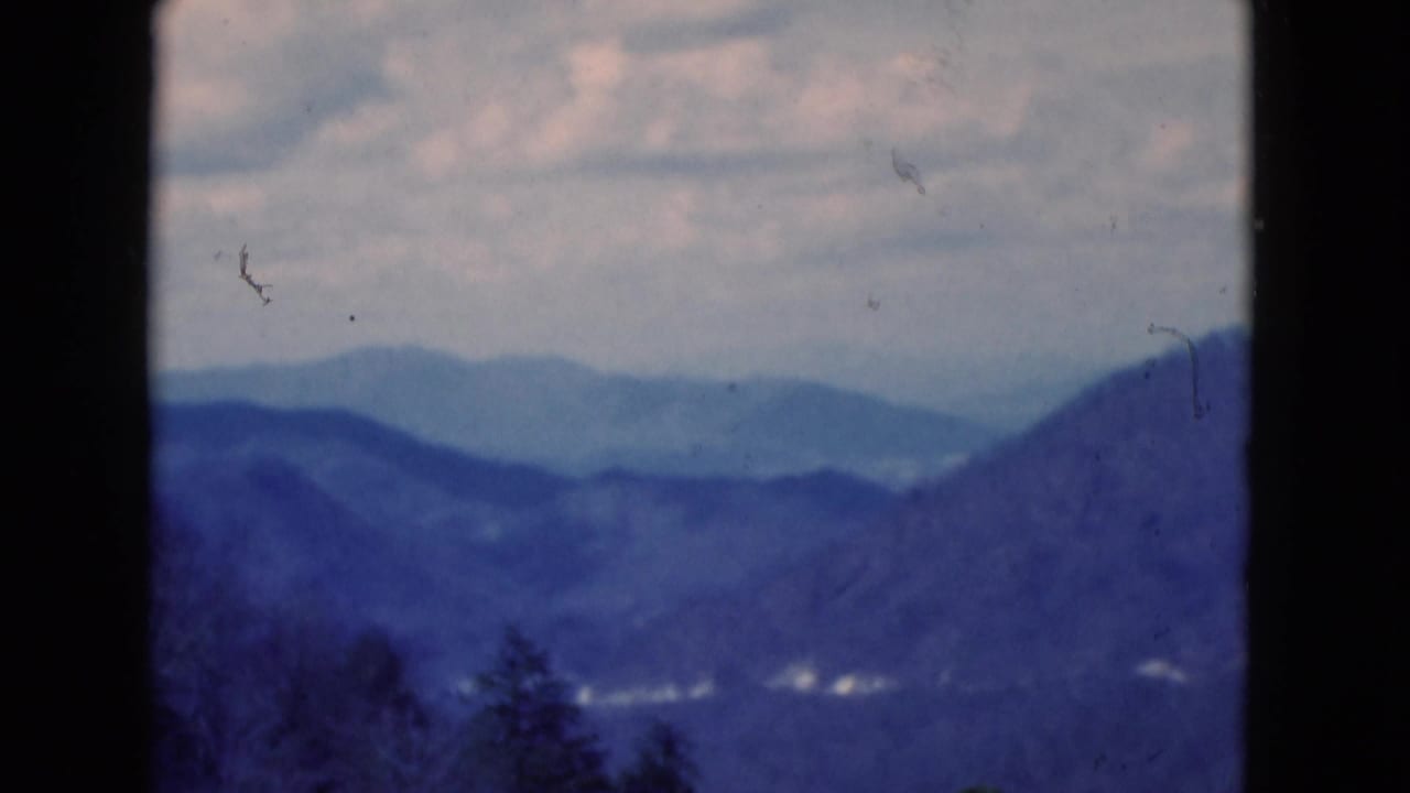 Cataloged 1975 8mm footage showing layered mountain ridges and a cloudy sky with dark frame edges and visible film wear.