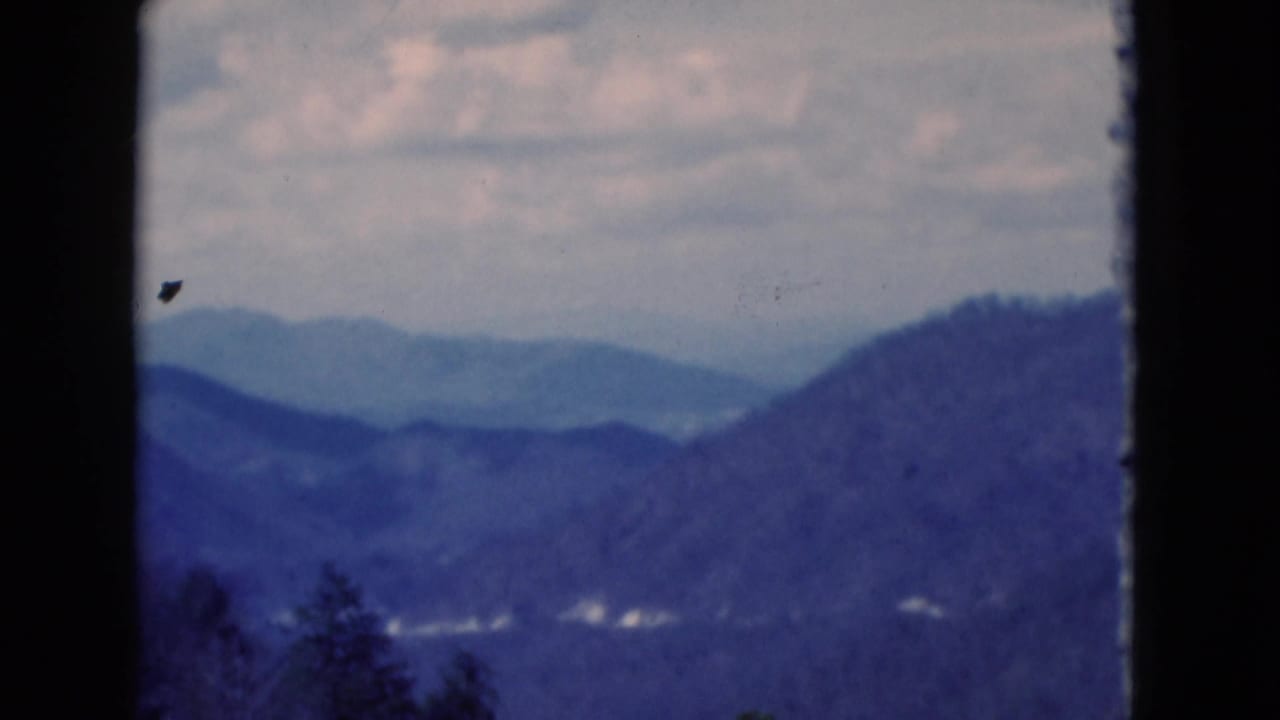 Blue-toned mountain vista with distant ridges, clouds, and dark film borders.