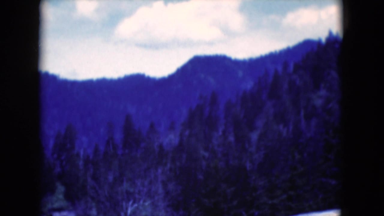 1975 8mm home-movie frame of a distant wooded hillside under pale sky, with a strong blue color cast and soft focus.