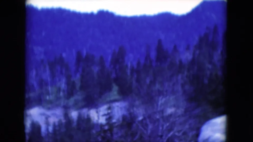 A soft 1975 8mm frame shows snow-covered ground, bare trees, and a wooded hillside with heavy blue color shift.