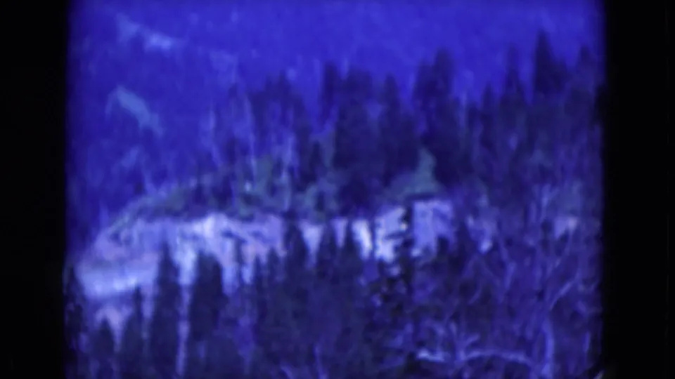 The final 1975 8mm frame shows a snowy wooded hillside and distant ridge, softened by grain, blur, and blue color shift.