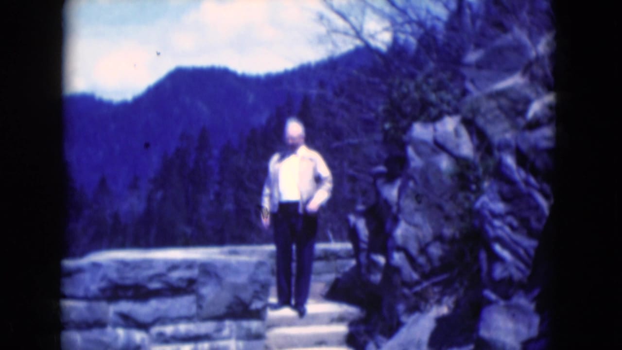 The man faces the camera area beside stonework and rocks, with blue-tinted wooded mountains behind him in the 1975 Florida clip.