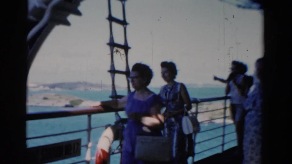 1975 Florida 8mm frame showing passengers by the railing, a vertical ladder, ocean water, and a partial life preserver on the boat deck.