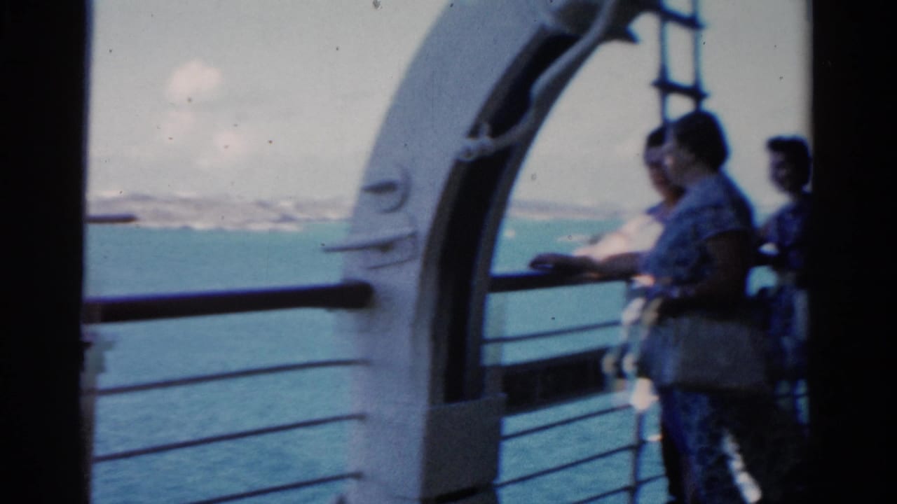 Passengers stand near the rail under a white ship arch with open water behind them.